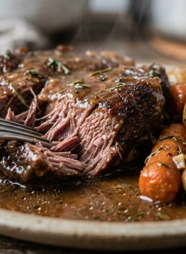 Extreme macro close-up of tender fork-shredded garlic herb pot roast glistening in savory gravy with caramelized baby carrots and potatoes