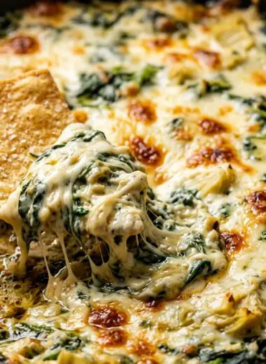 Extreme macro close-up of hot bubbly baked spinach artichoke dip in cast iron skillet with golden blistered melted cheese and crispy tortilla chip scooping with cheese pull